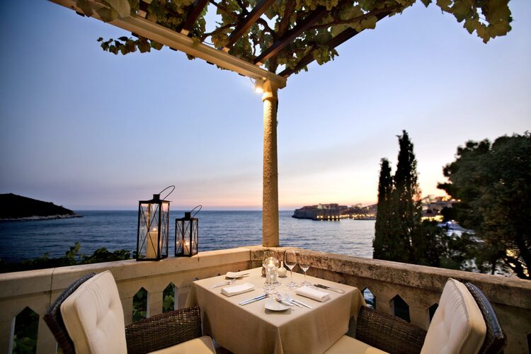 Victoria Restaurant on the Croatian coast rustic terrace with lanterns overlooking a bat with two white chairs and a small table prepared for dinner