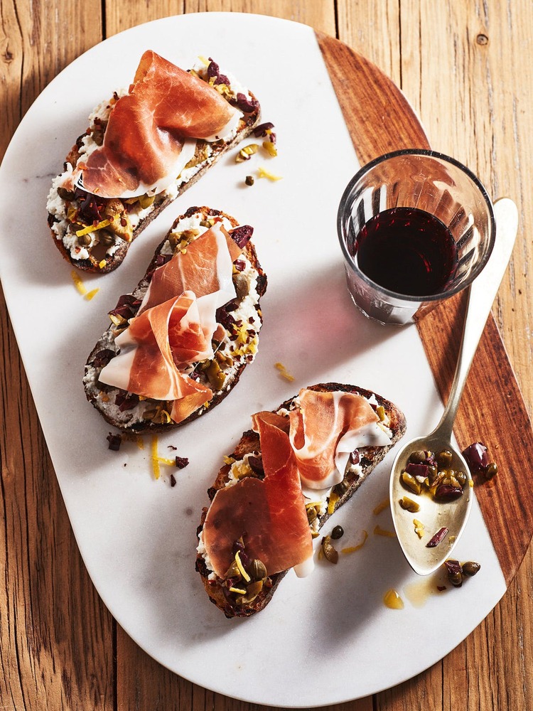bruschette on a white platter with a glass of red wine on a wooden table surface