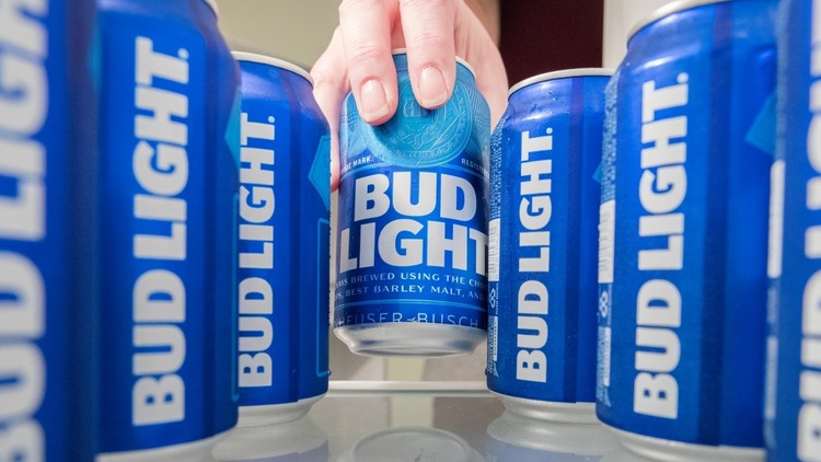 bud light beer ad glass shelf with several blue cans of beer hand picking one can in the background