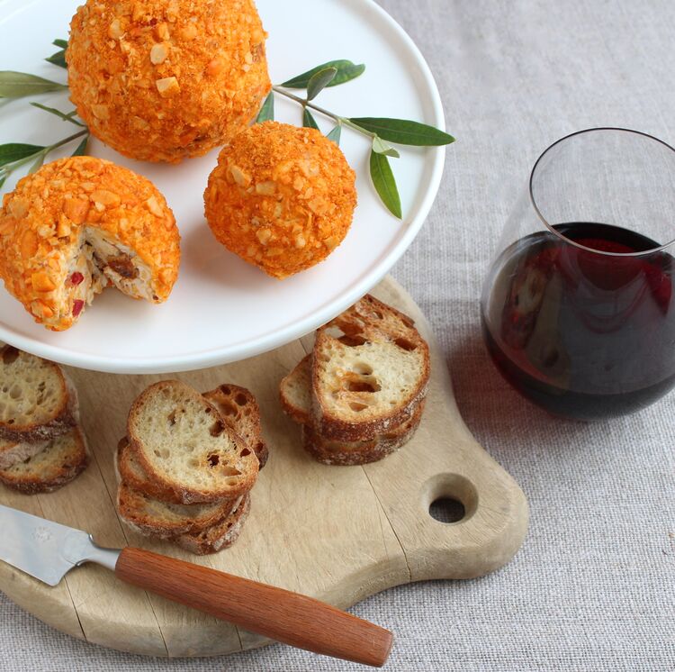 cheese balls looking like tangerines with small crostini and a glass of red wine on a wooden cutting board