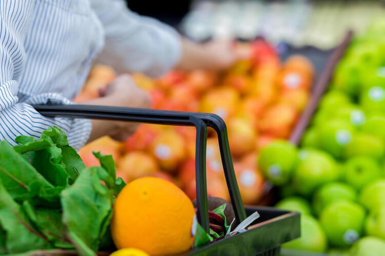 woman in white and blue shirt holding a shopping basket and picking fruits in a supermarket