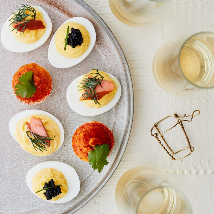 deviled eggs with different decorations on a plate with glasses of champagne around