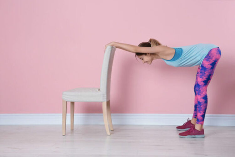 Young woman exercising with chair near a pink wall
