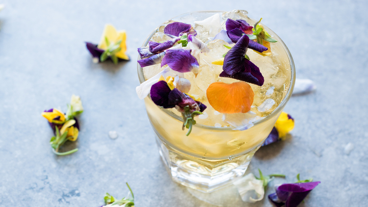 herbal cocktail in a glass with crushed ice and edible flowers in it