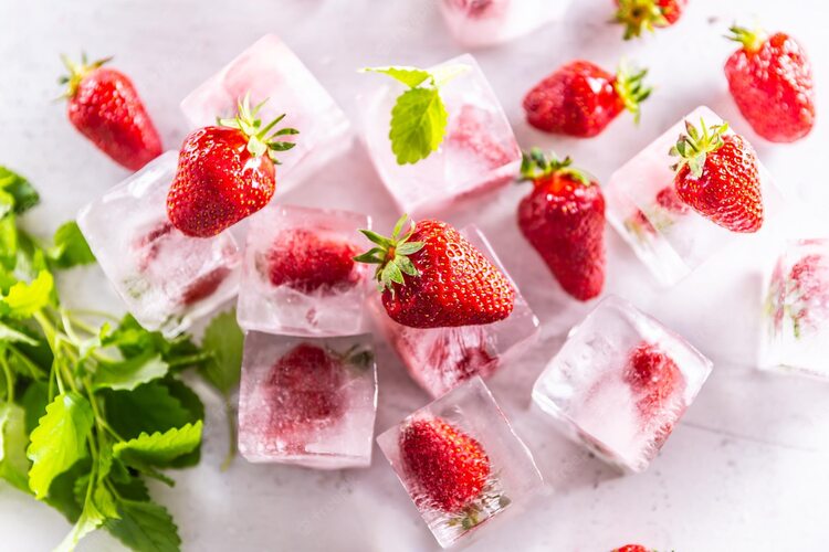 frozen strawberry ice cubes with green mint leaves scattered around on a light surface