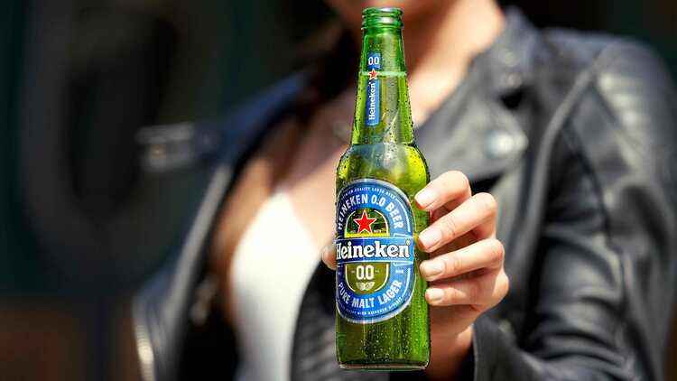 woman in a leather jacket holding a bottle of heineken showing it to the camera