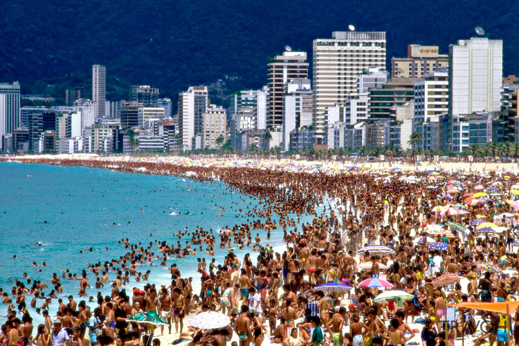 ipanema beach in Brazil with crowds sunbathing and swimming and tall buildings in the background 