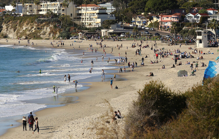 laguna beach in the USA with few people on it and buildings in the background