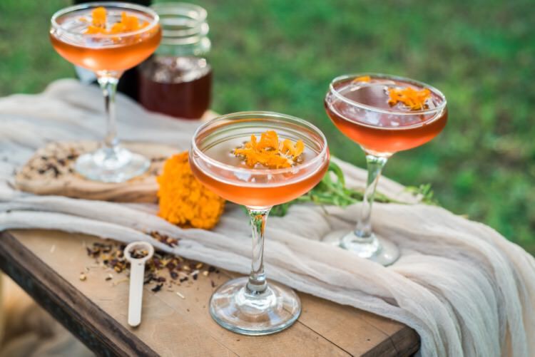 three marigold cocktails outdoors on a wooden table with flowers in them