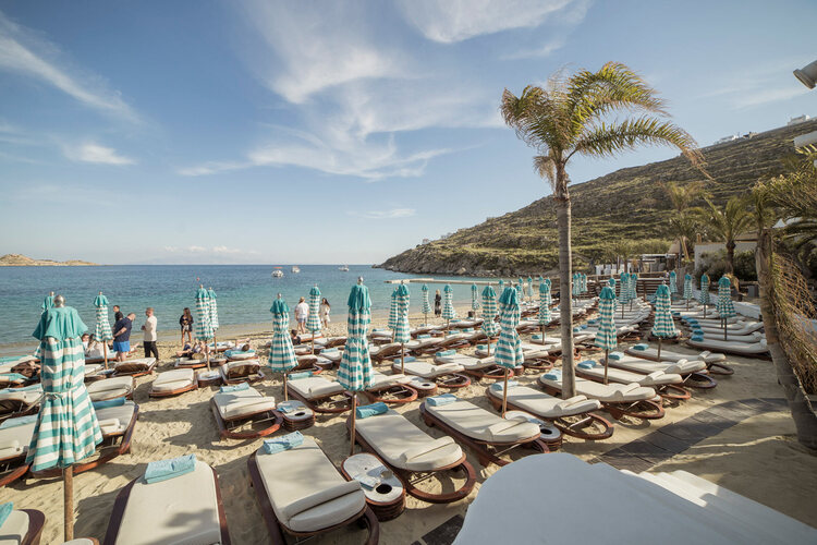 Nammos beach with lounge chairs and blue and white parasols and a single palm tree