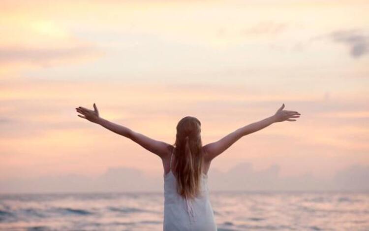 stress relief woman at the beach with the sea in the background spreading her hands towards the sky