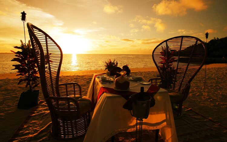 two tall chairs on the beach and a decorated table with a beautiful sunset in the background