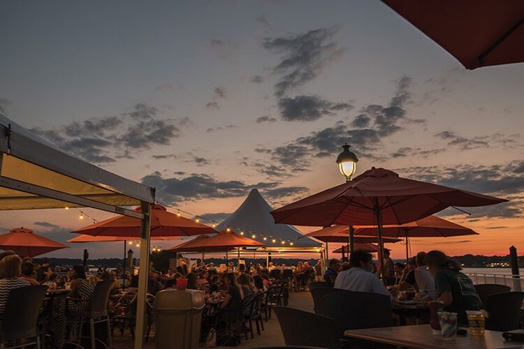 bar with parasols and lights and people sitting and dining with a sunset in the sky