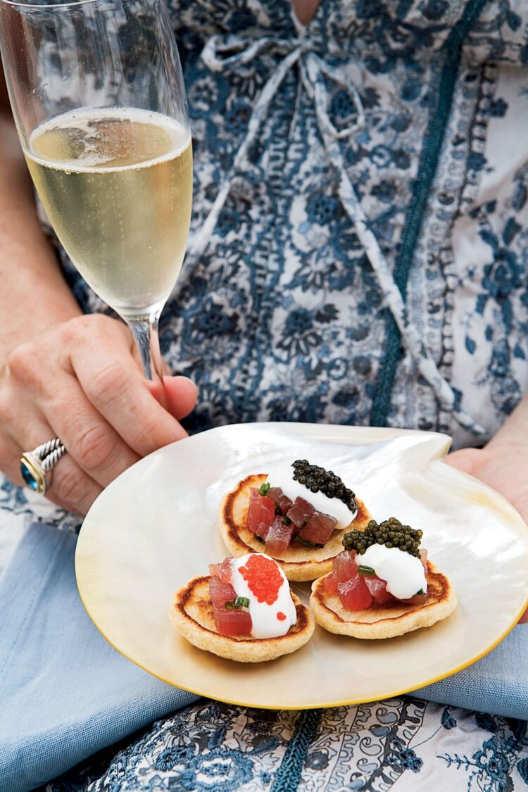 woman in a blue and white dress holding a champagne glass and a plate with appetizers