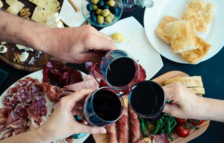 wine appetizers three hands holding glasses with red wine over a table covered in different appetizers