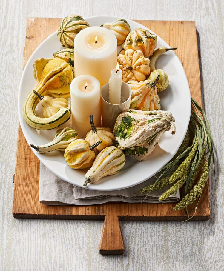 fall themed table decor with gourds and candles on a wooden cutting board