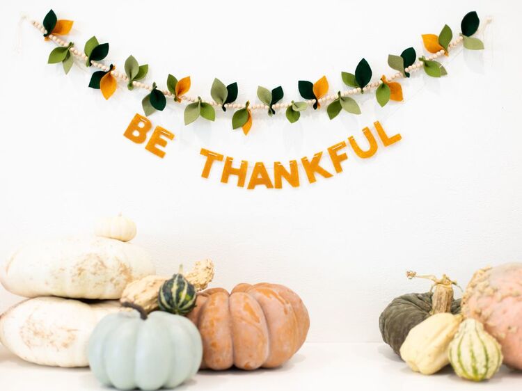 festive garland with the words be thankful hanging on a wall with decorative pumpkins under it