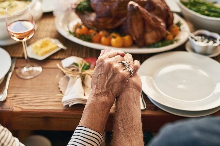 two elderly people holding hands in prayer over a thanksgiving table