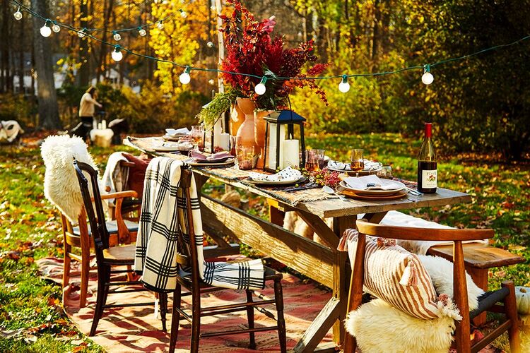 thanksgiving table setting outdoors with blankets on the chairs and fairy lights