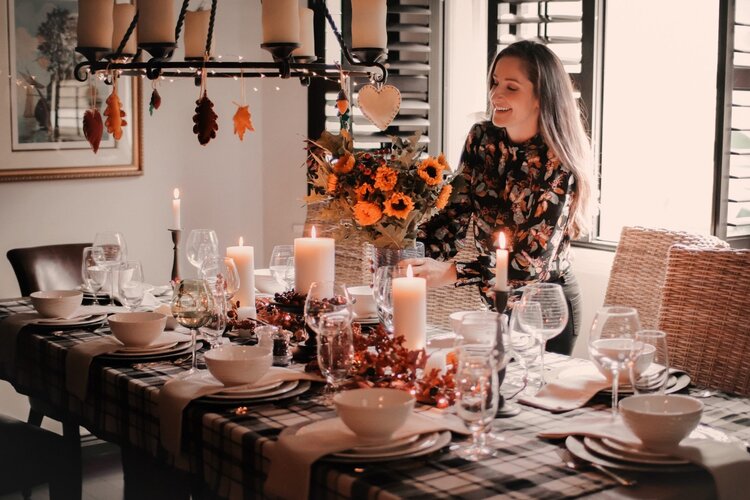 thanksgiving table woman smiling and putting a floral centerpiece in a decorated room