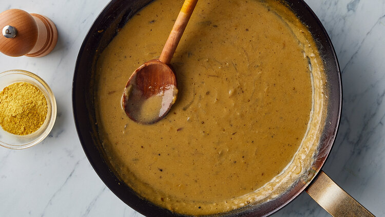 umami gravy in a large pot with a wooden spoon in it and some spices next to it on a white table 